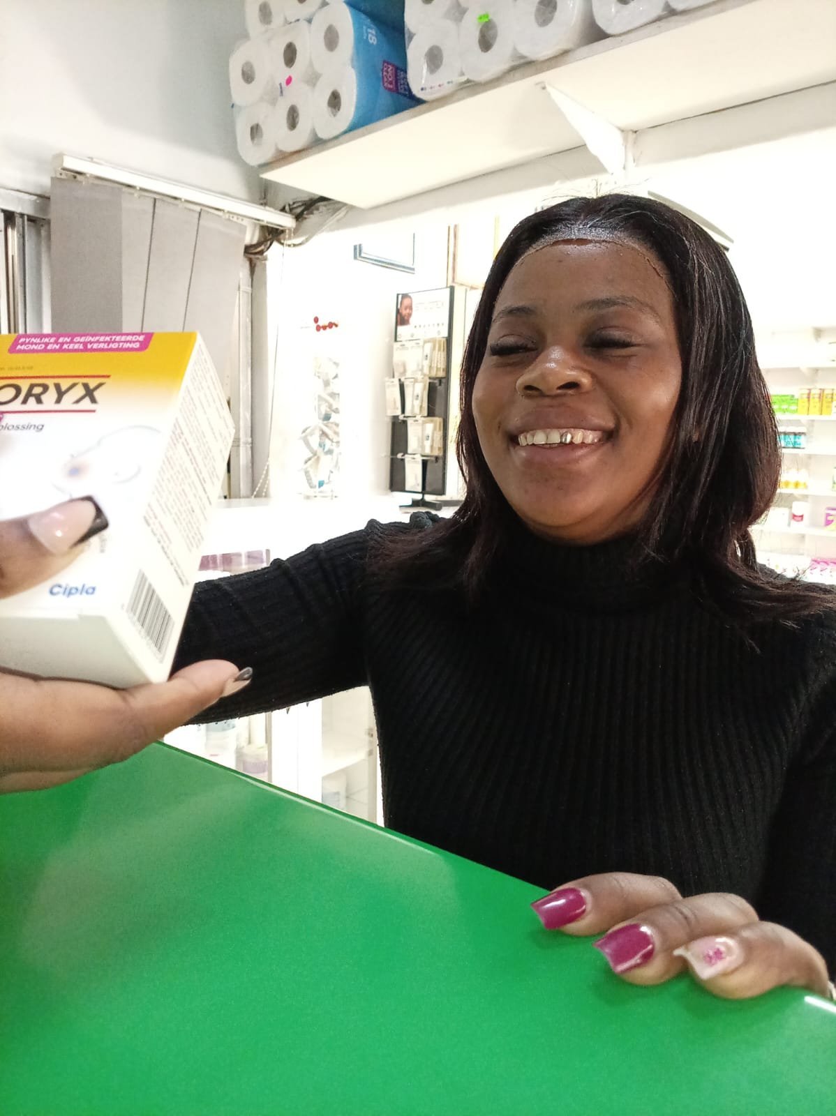 Smiling woman holding a box of Oryx product at a store counter with shelves of supplies in background