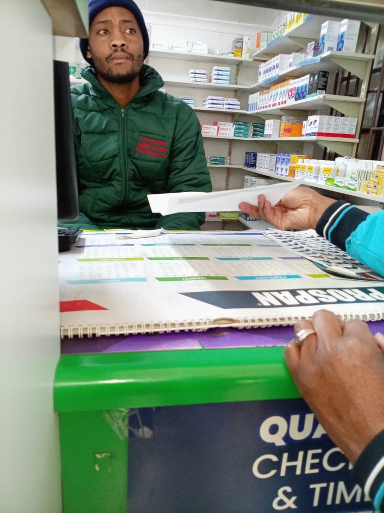 Man in green jacket and blue beanie at pharmacy counter with customer holding documents, shelves of medications in background